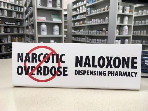 Naloxone pharmacy sign on counter showing the pharmacy now sells over the counter naloxone injections to prevent drug overdose